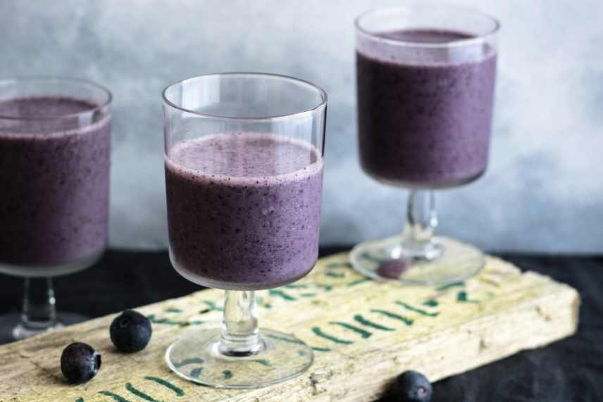 An image of three glasses of Blueberry Spinach Smoothies on a wooden board.