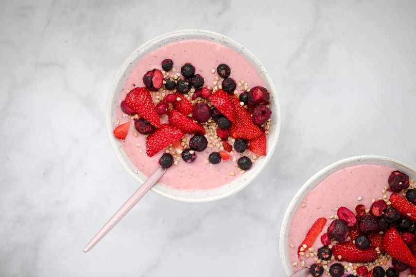 Two mixed berry smoothie bowls on a white marble counter top.