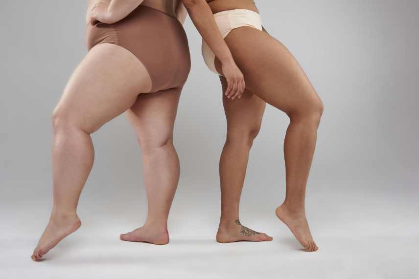 A photo of 2 women from the waist down. Both are wearing beige leg garments. One of the women is overweight.