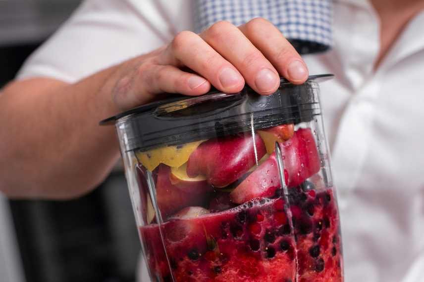 A woman holding down the lid of a blender as she prepares a mixed fruit smoothie for weight loss.