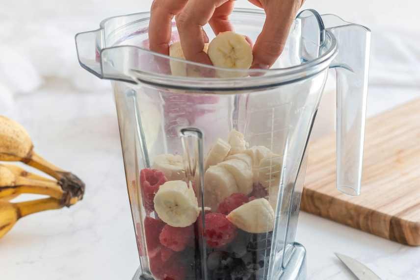 An image of a blender with a person loading it with fresh fruits to make Vegan Protein Smoothies.