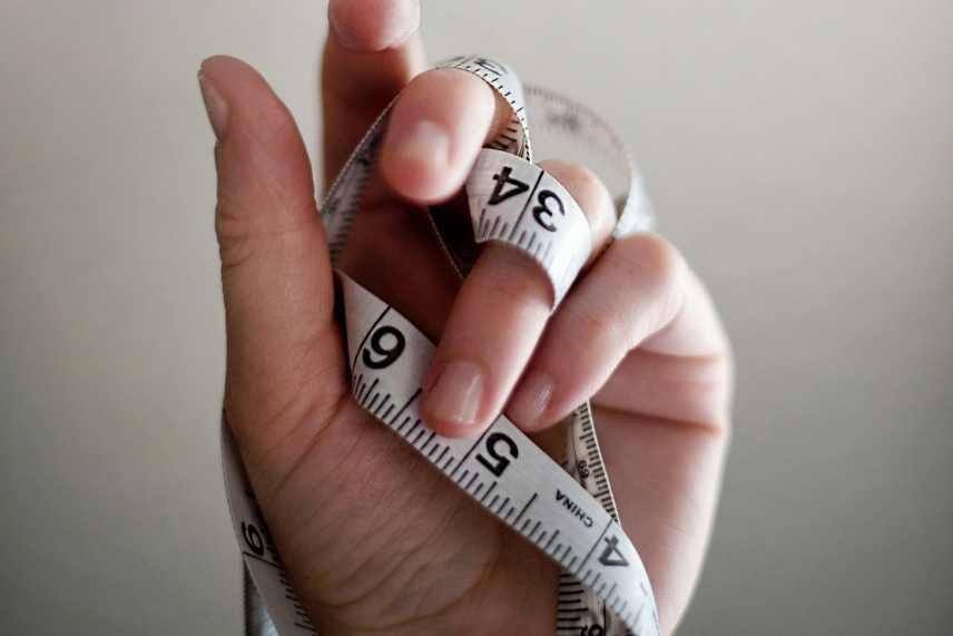 A tape measure wrapped around  a hand. The benefits of regular physical activity for weight loss can be measured and recorded.